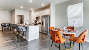 A modern kitchen with a central island, stainless steel appliances, and a dining area with orange chairs. - 5 Mi to Fort Harrison: Home w/ Pool Access! (McCordsville)