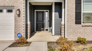 A house with a garage door, a front door, and a small garden area with plants. - 5 Mi to Fort Harrison: Home w/ Pool Access! (McCordsville)