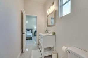 A narrow hallway leading to a bedroom with a bed and nightstand. A bathroom with a sink, mirror, and toilet is visible to the right. - Walk to Guadalupe River: Seguin Home w/ Fire Pit (Seguin)