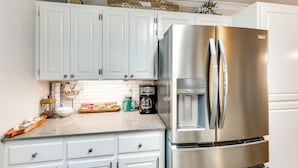 Una cocina con armarios blancos, un refrigerador de acero inoxidable, una cafetera y un cartel sobre los armarios.