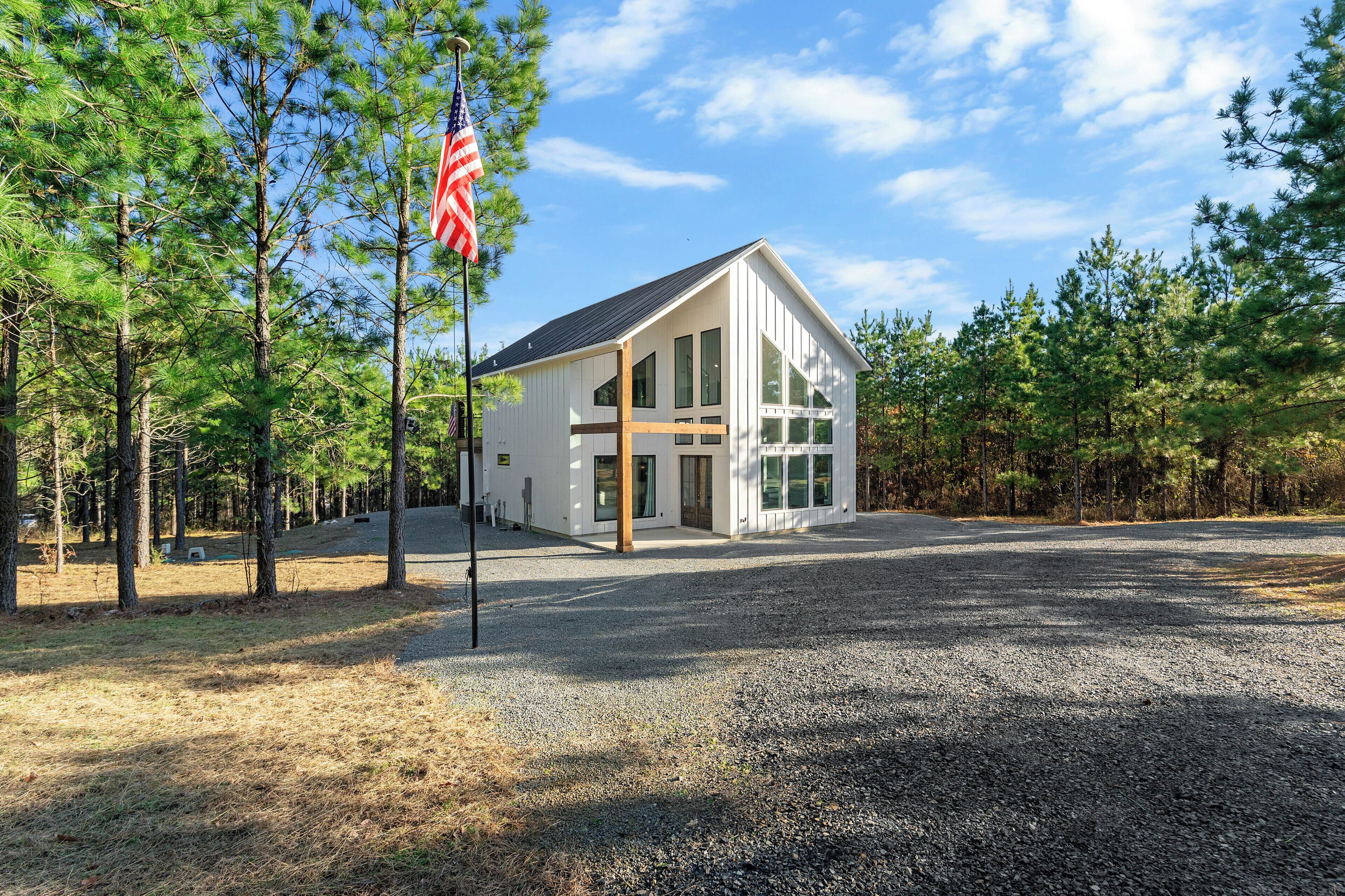 A modern building with large windows, surrounded by a gravel driveway and pine trees.