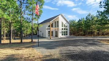 A modern building with large windows, surrounded by a gravel driveway and pine trees.