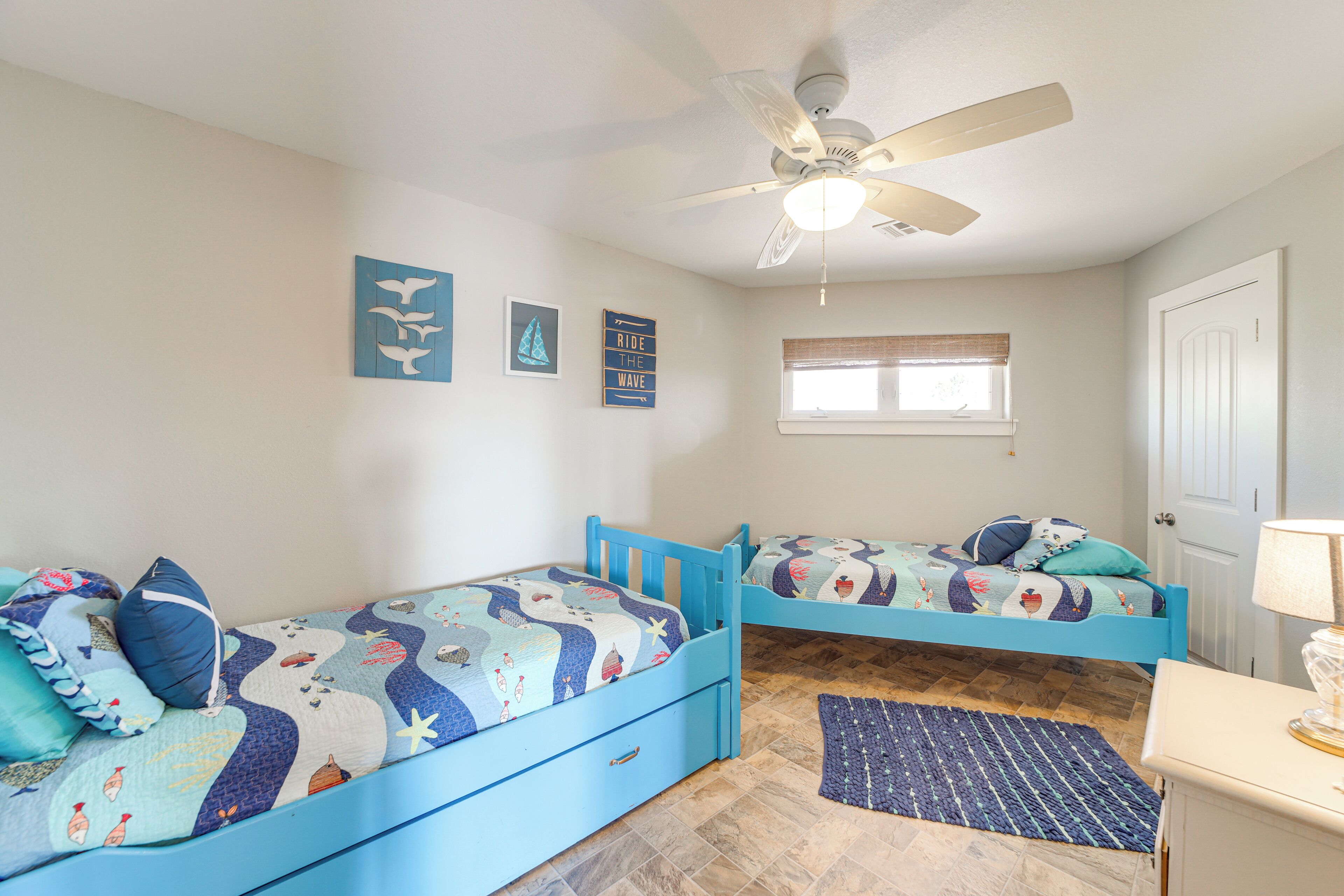 A bedroom with two blue beds, a ceiling fan, and a window with blinds.