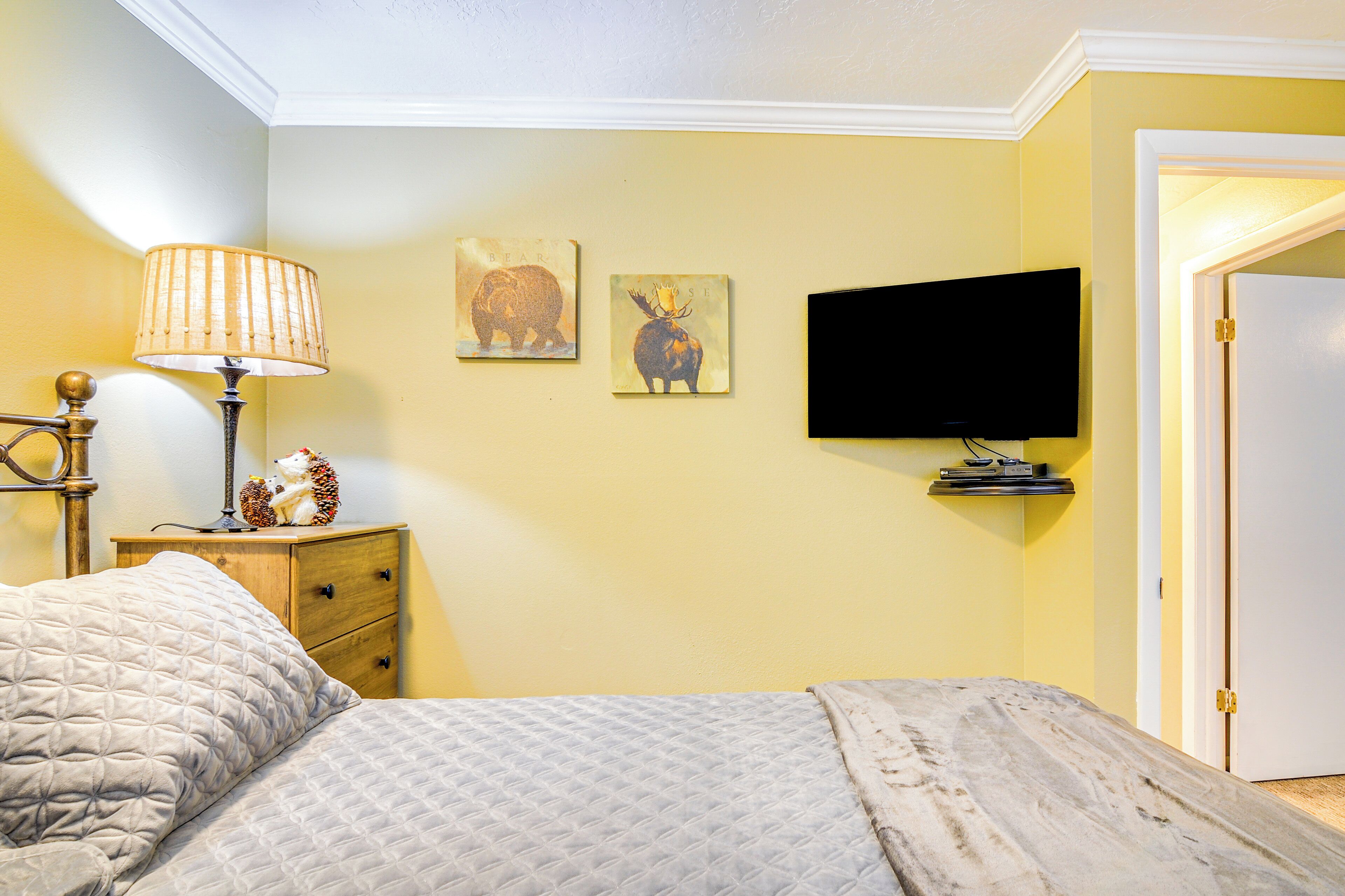 A bedroom with a bed, a bedside lamp, a television, and two wall art pieces.