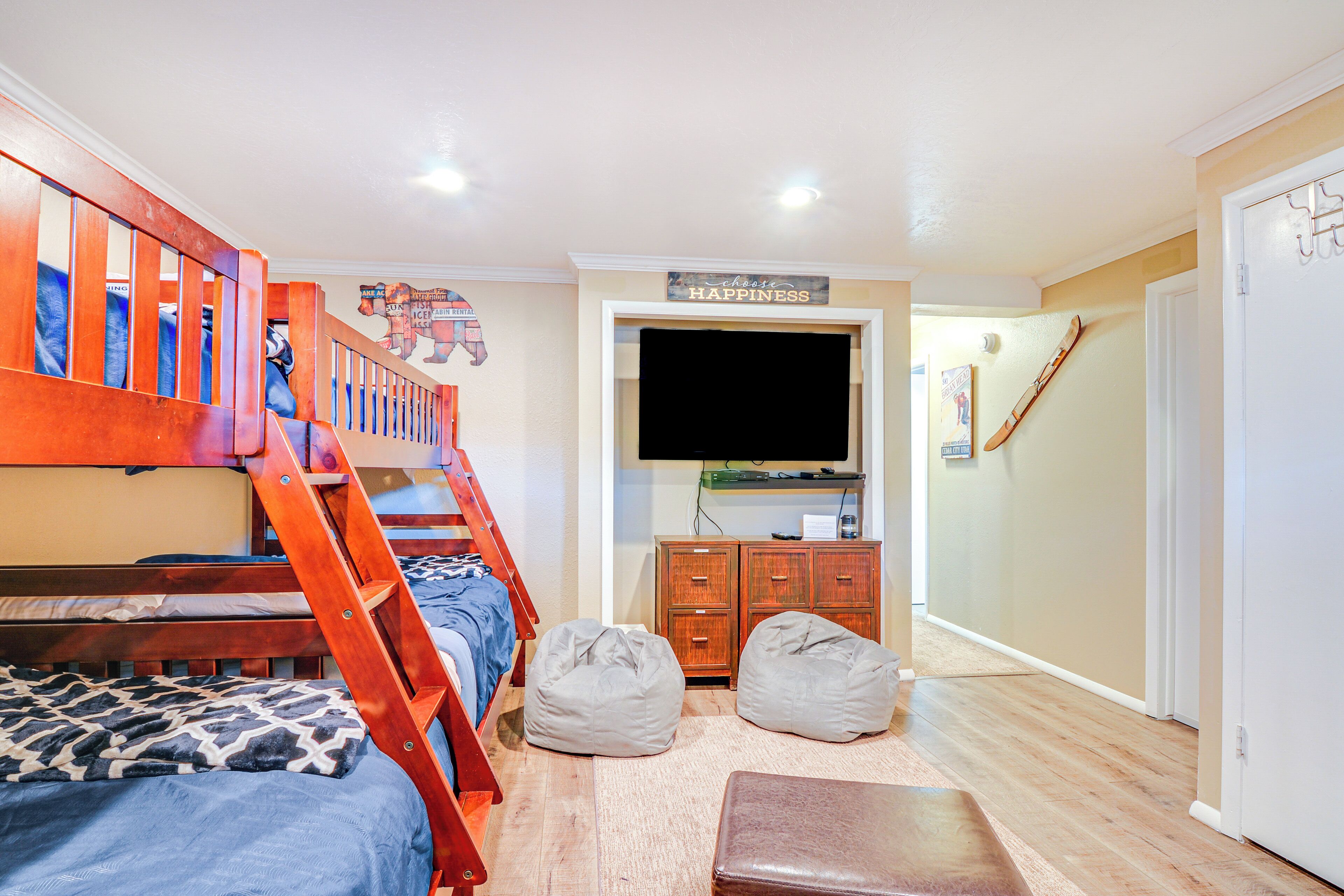 A room with a bunk bed, a desk with a computer, a television, and a door with a coat hanging on it.