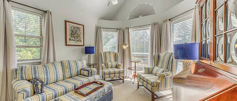 A living room with a striped sofa, armchairs, a coffee table, and a wooden cabinet.