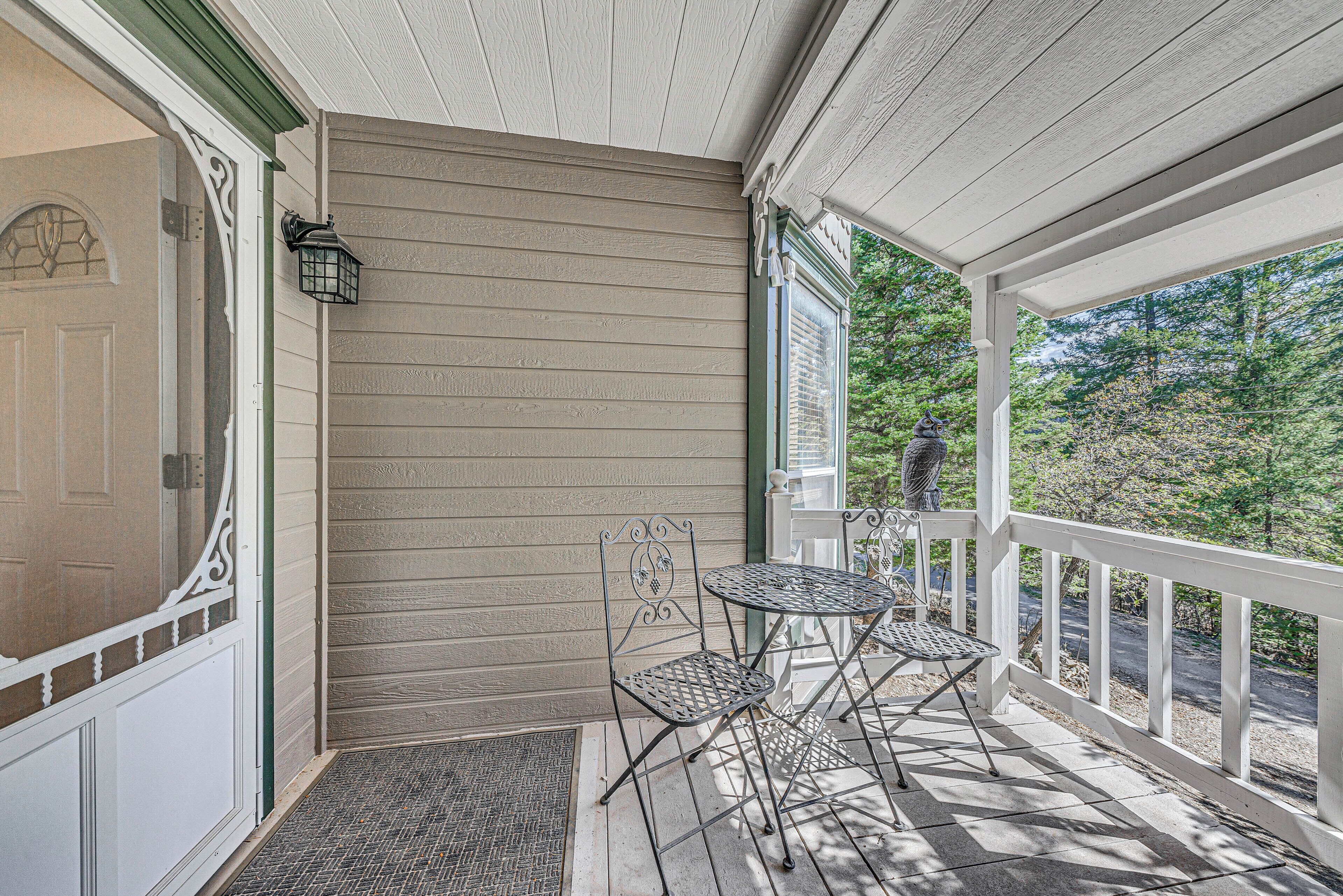 A covered porch with a table and chairs, a door, and a view of the surrounding trees.