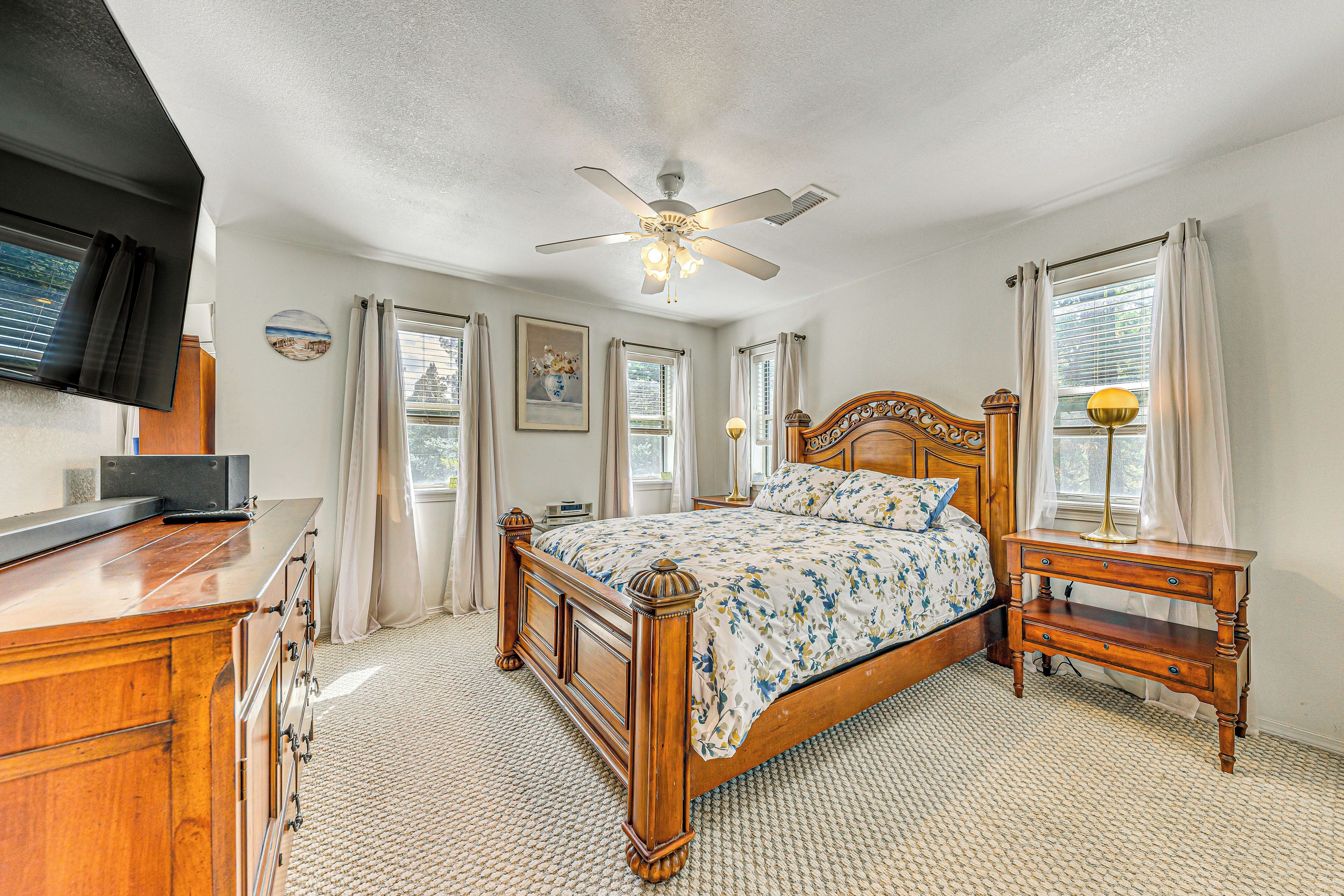 A bedroom with a wooden bed, a nightstand, a ceiling fan, and a television on the wall.