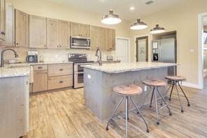 A kitchen with wooden cabinets, a granite countertop, a stainless steel refrigerator, and a central island with stools. - Scenic Views, Fire Pit: Texas Hill Country Getaway (Fischer)