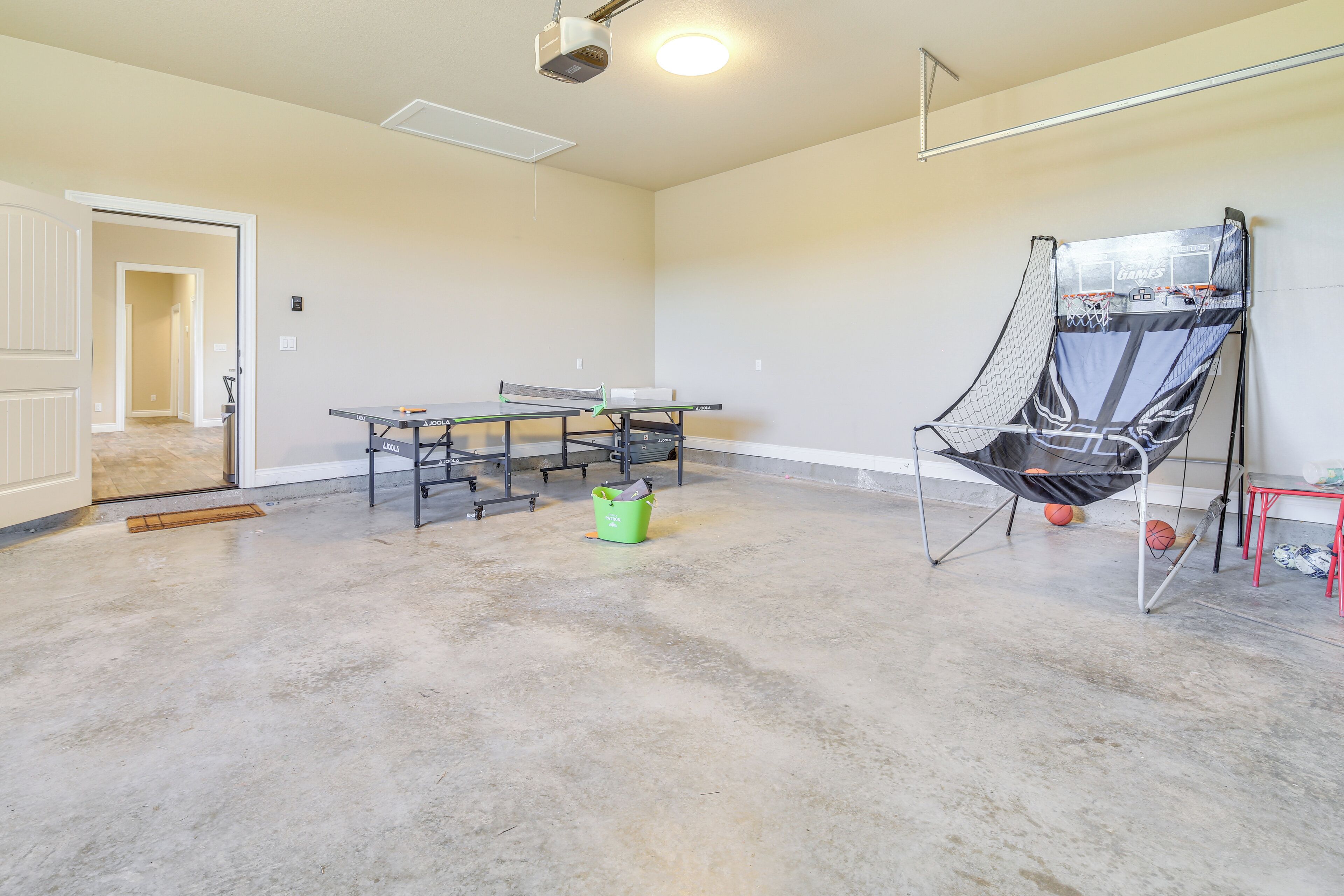 En rummelig stue med et pingpongbord, en basketballkurv og en dør til et andet område.