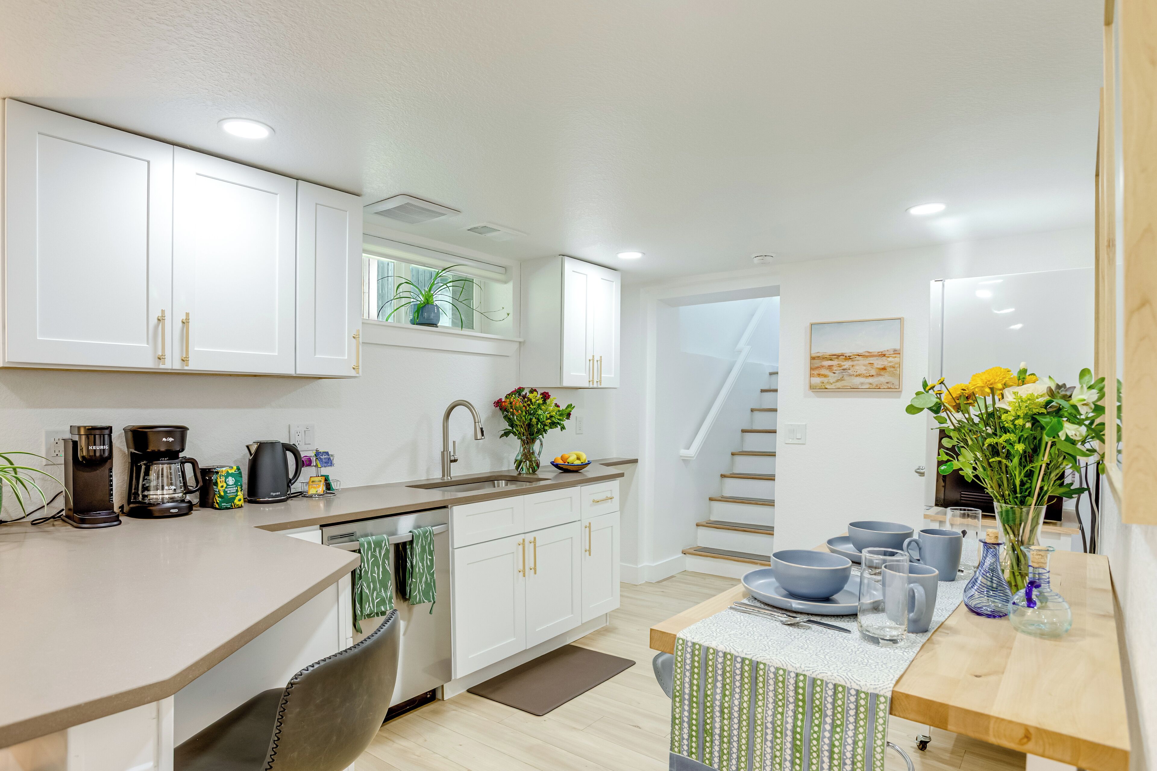 A modern kitchen with white cabinets, a coffee maker, and a dining area with a table set for two.