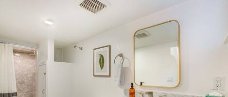A bathroom with a white toilet, a shower, a marble sink, and a mirror with a gold frame.