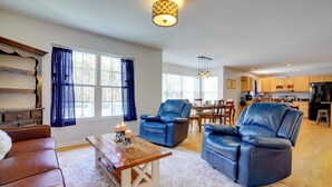 A spacious living room with a brown leather sofa, a blue leather armchair, and a wooden coffee table with candles. A dining area with a table and chairs is visible in the background. - Group Getaway ~ 15 Mi to Charlottesville! (Troy)