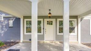 A covered porch with a white door and windows, a light fixture above, and a brick wall to the left. - 5 Mi to Lake: Port Clinton Home w/ Gazebo & Grill! (Port Clinton)