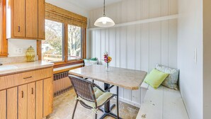 A kitchen with wooden cabinets, a large window, a dining table, and a hanging light fixture.