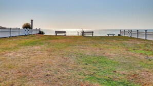 A grassy area with two benches facing a body of water, enclosed by a white fence.