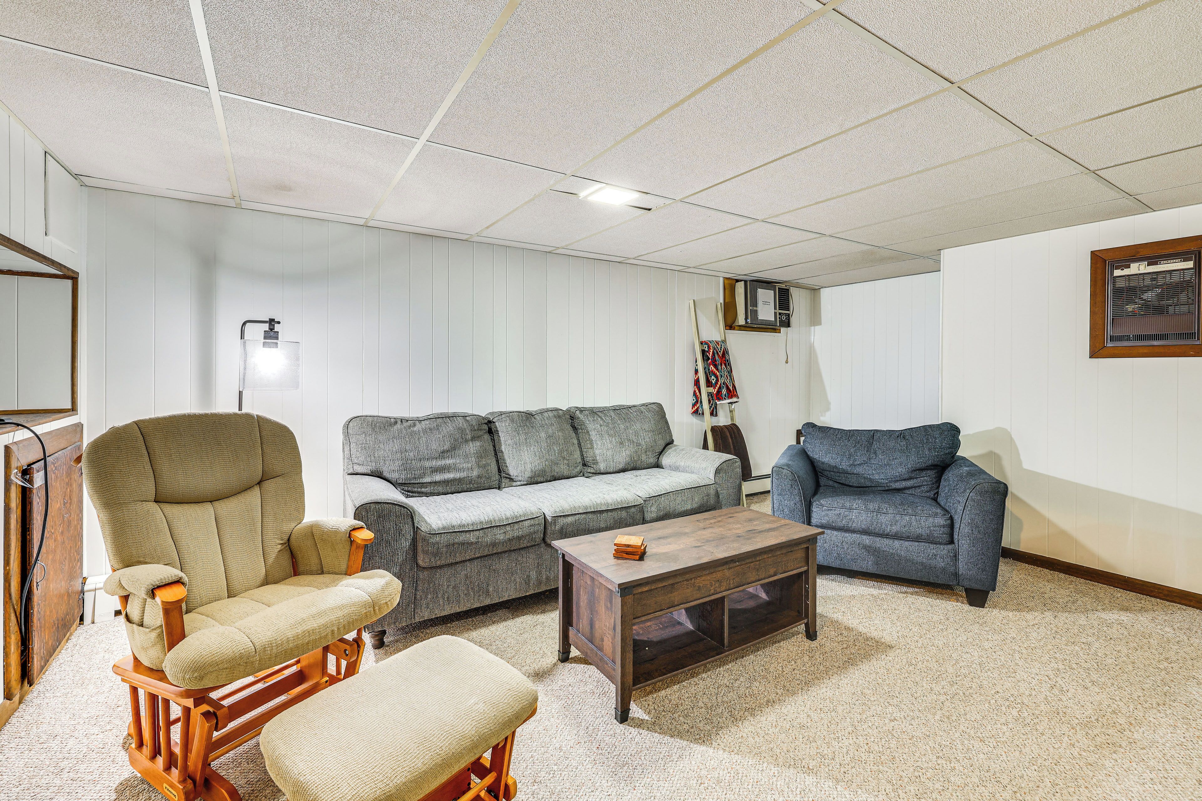 A living room with a wooden rocking chair, a grey sofa, and a blue sofa. There is a wooden coffee table and a lamp on a side table.
