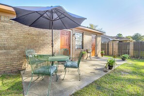 A patio with a table and chairs, a black umbrella, and potted plants. - Patio for Al Fresco Dining: Home in Hinesville! (Hinesville)