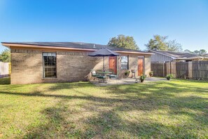 A single-story brick house with a patio, a wooden fence, and a clear blue sky. - Patio for Al Fresco Dining: Home in Hinesville! (Hinesville)