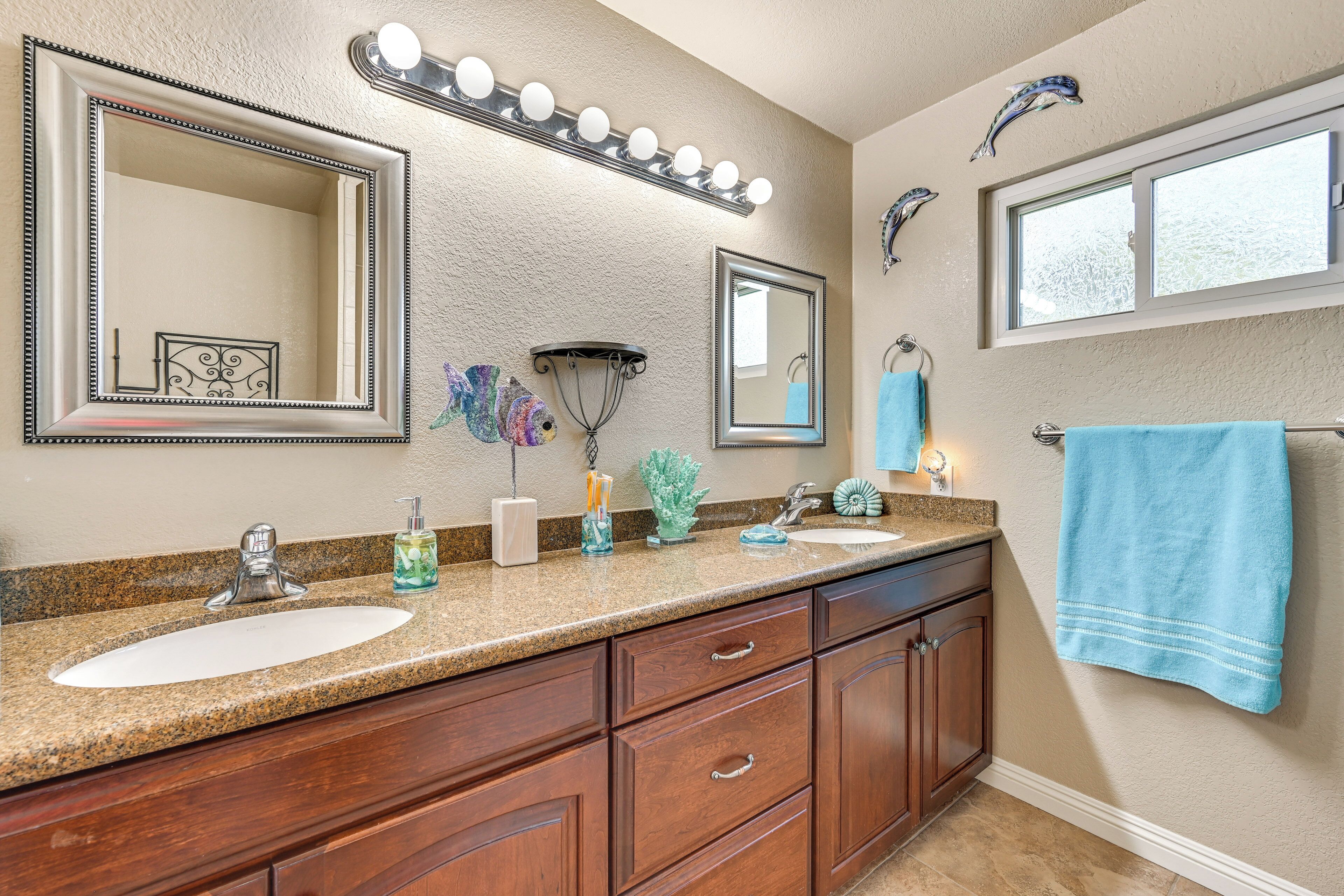 A bathroom with two sinks, vanity cabinets, a large mirror, and a window.