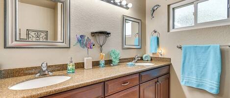 A bathroom with two sinks, vanity cabinets, a large mirror, and a window.