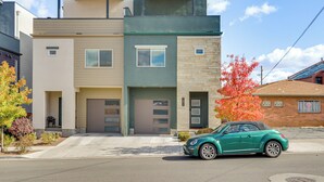 Een modern woonhuis met twee verdiepingen, een garage, een groene auto ervoor en een boom met rode bladeren aan de rechterkant.