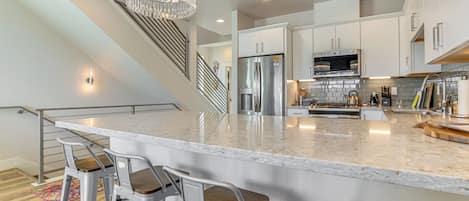 A modern kitchen with a large island, stainless steel appliances, and a staircase.