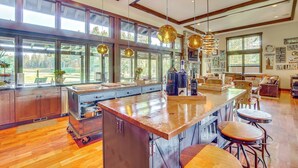 A spacious kitchen with a large island, wooden cabinets, and a view of the outdoors through large windows. - Golf Getaway w/ Hot Tub, Course Views in Cle Elum! (Cle Elum)