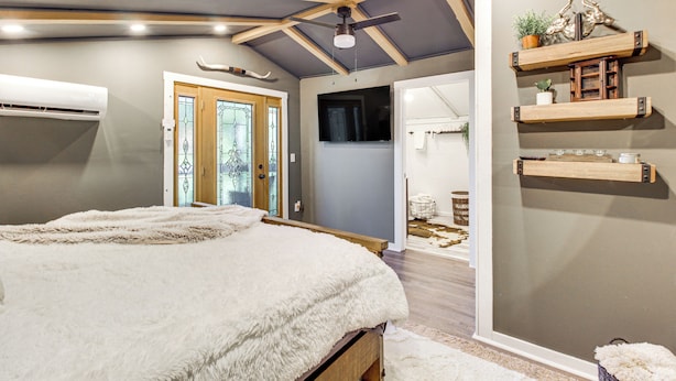 Ein Schlafzimmer mit einem großen Bett, Holzbalken an der Decke, einem Deckenventilator und einem an der Wand befestigten Regal mit Dekoration.