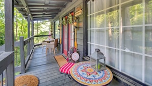 Eine überdachte Veranda mit Tisch und Stühlen, einem Willkommensschild und Blick auf den Wald.