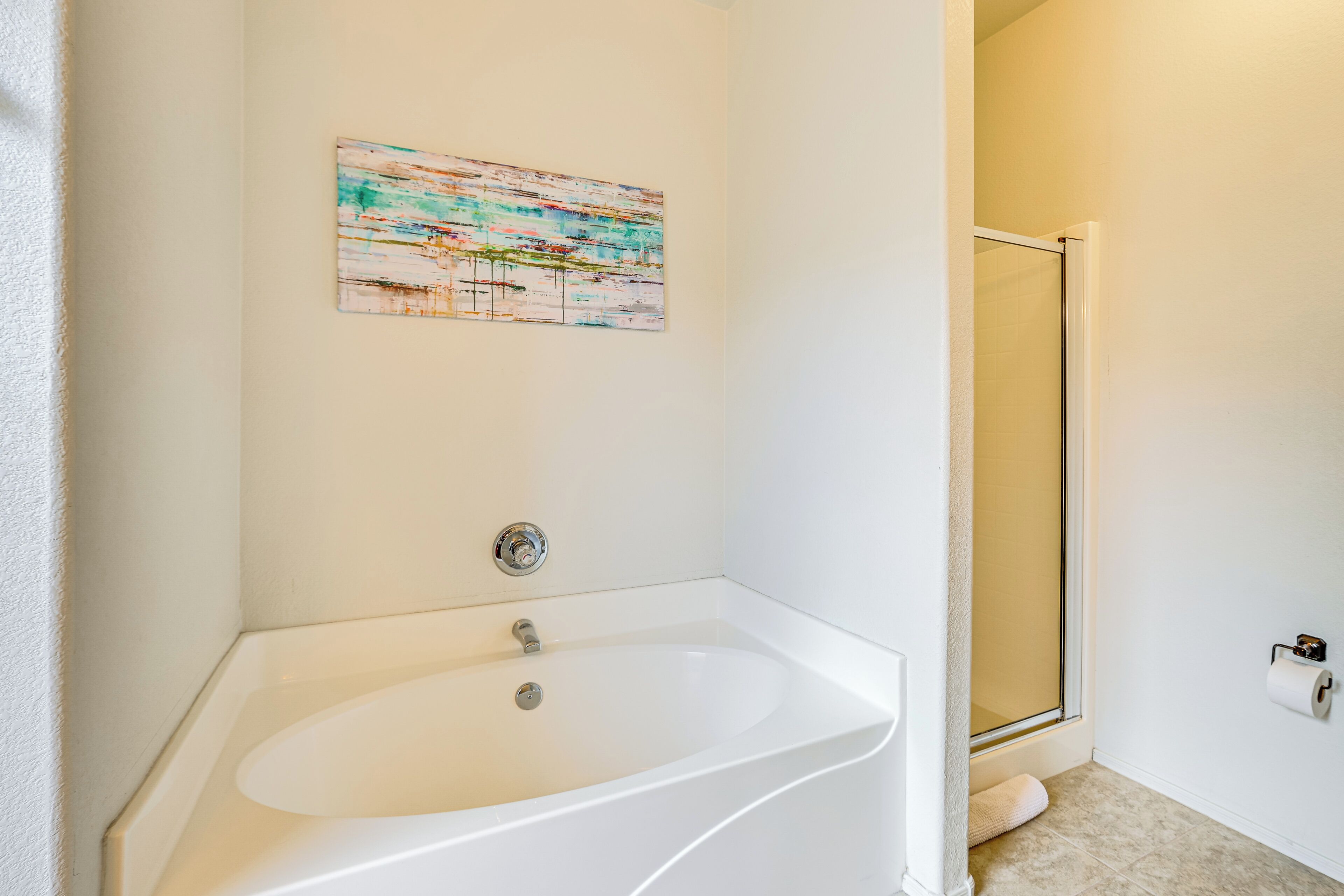 A bathroom with a white bathtub, a glass shower enclosure, and a single roll of toilet paper on the wall.