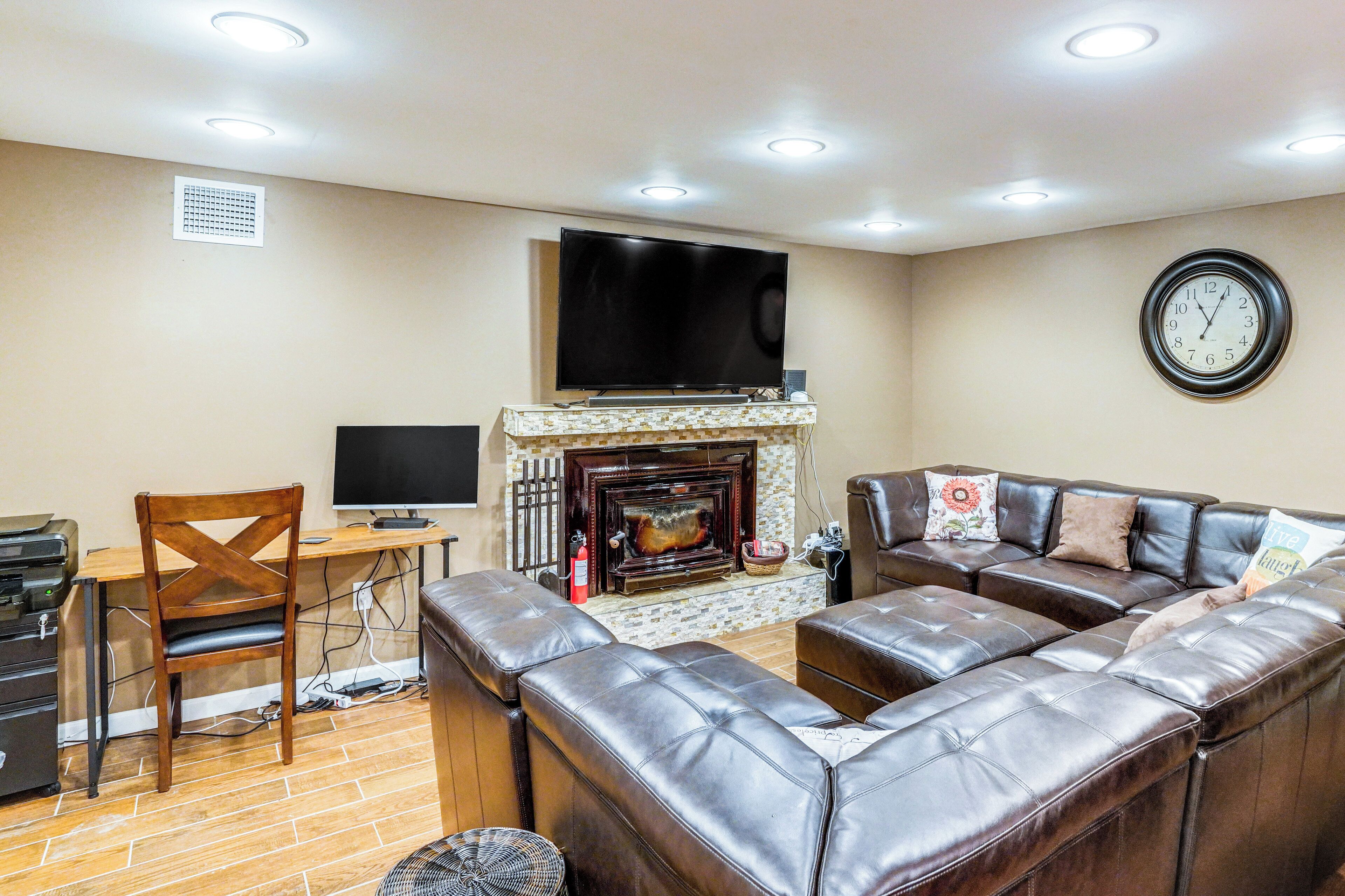 A living room with a fireplace, leather sofa, TV, and a clock on the wall.