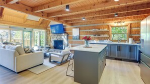 A modern kitchen with a stone fireplace, wooden beams, and large windows. - 3 Mi to Dtwn: Mtn-view Cabin in Gatlinburg! (Gatlinburg)