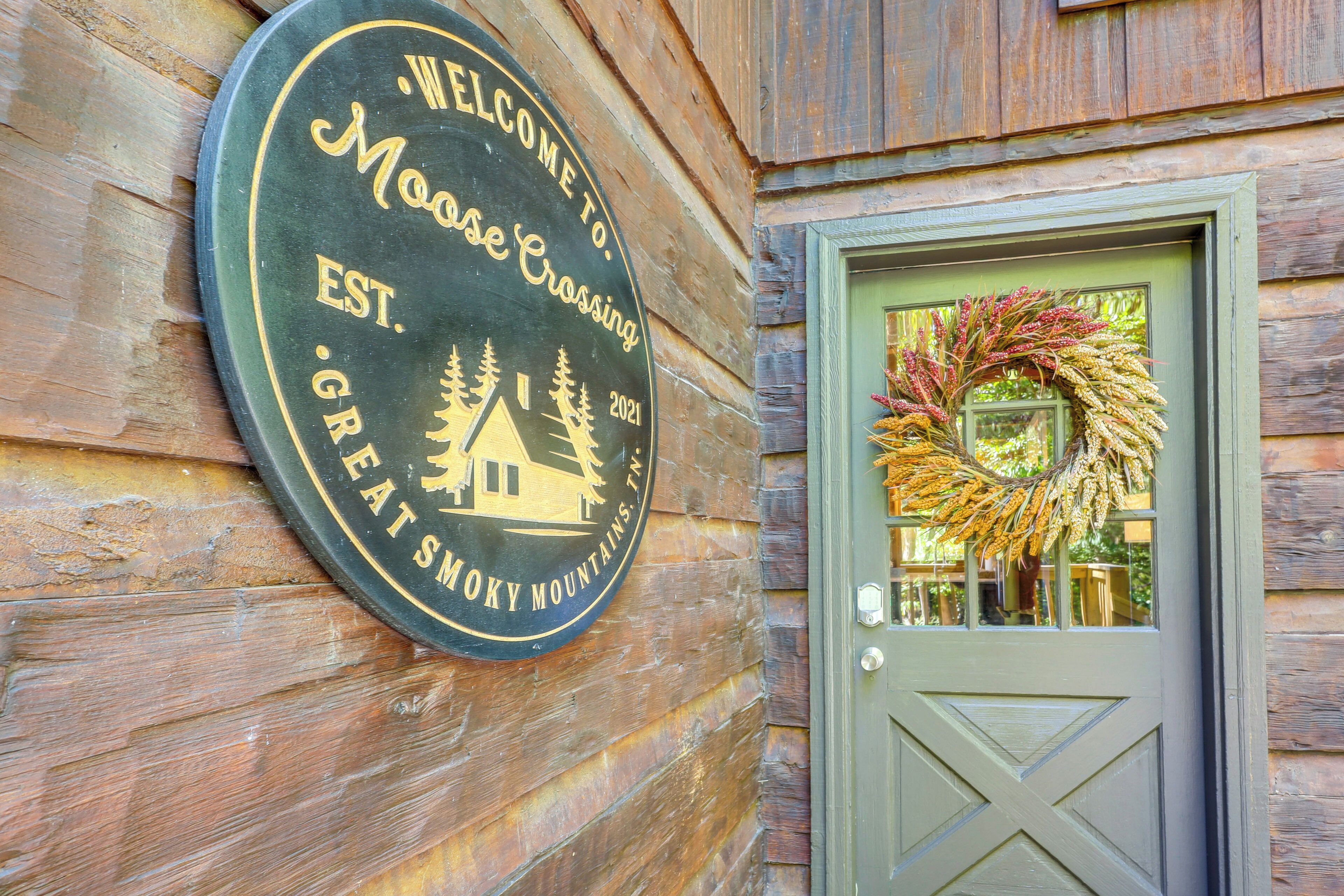 A wooden wall with a circular sign reading "Welcome to Moose Crossing, Established 2021, Great Smoky Mountains."
