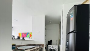 Une cuisine compacte équipée d’un lave-linge, d’un réfrigérateur et d’un plan de travail avec un évier.