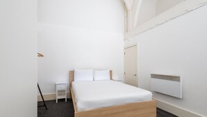 A minimalist bedroom with a wooden bed, white bedding, a small bedside table, and a wall-mounted heater. - Host Stay City Hall View (Sheffield)