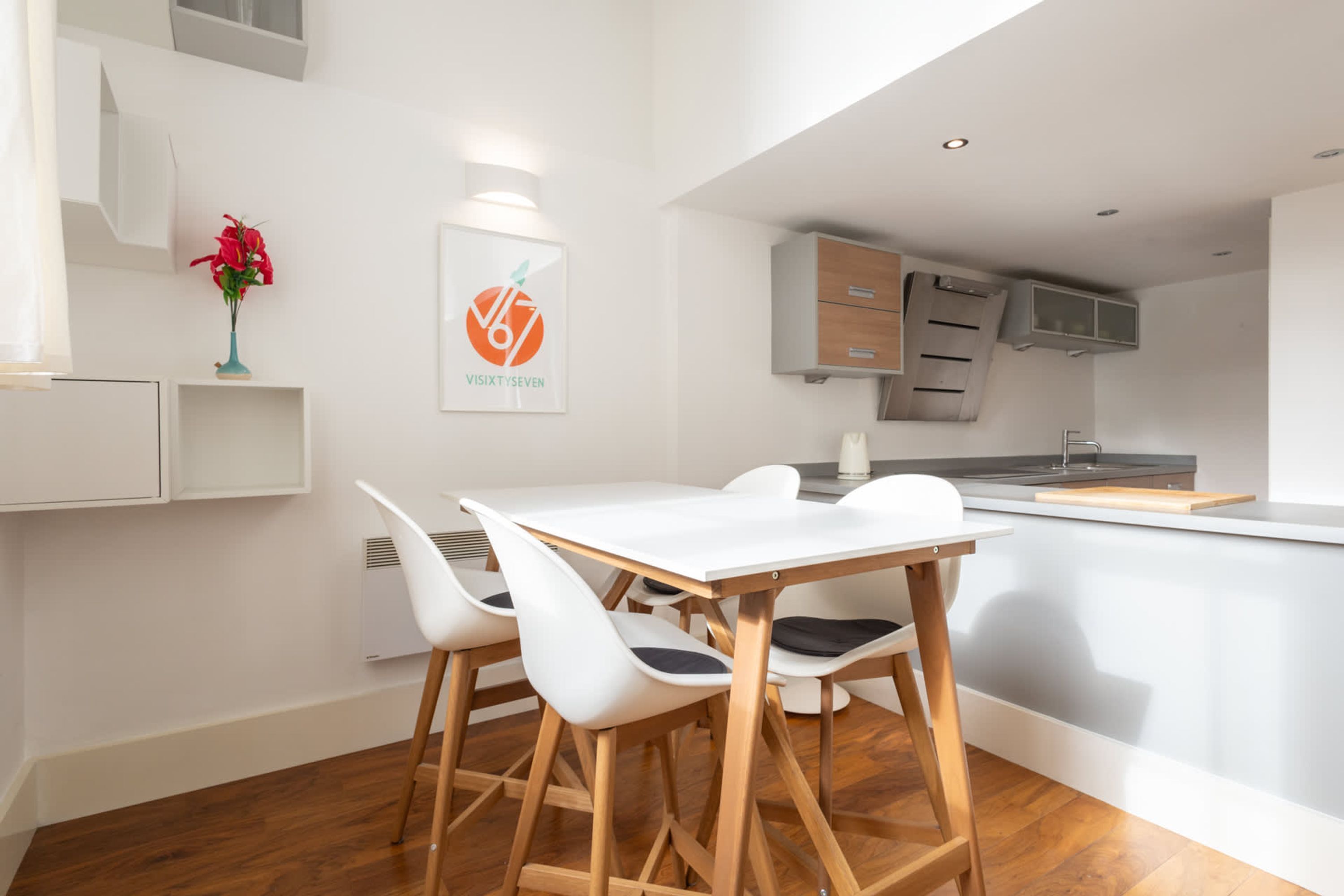 A modern kitchen with white cabinetry, a white dining table with four chairs, and a small island with a sink.