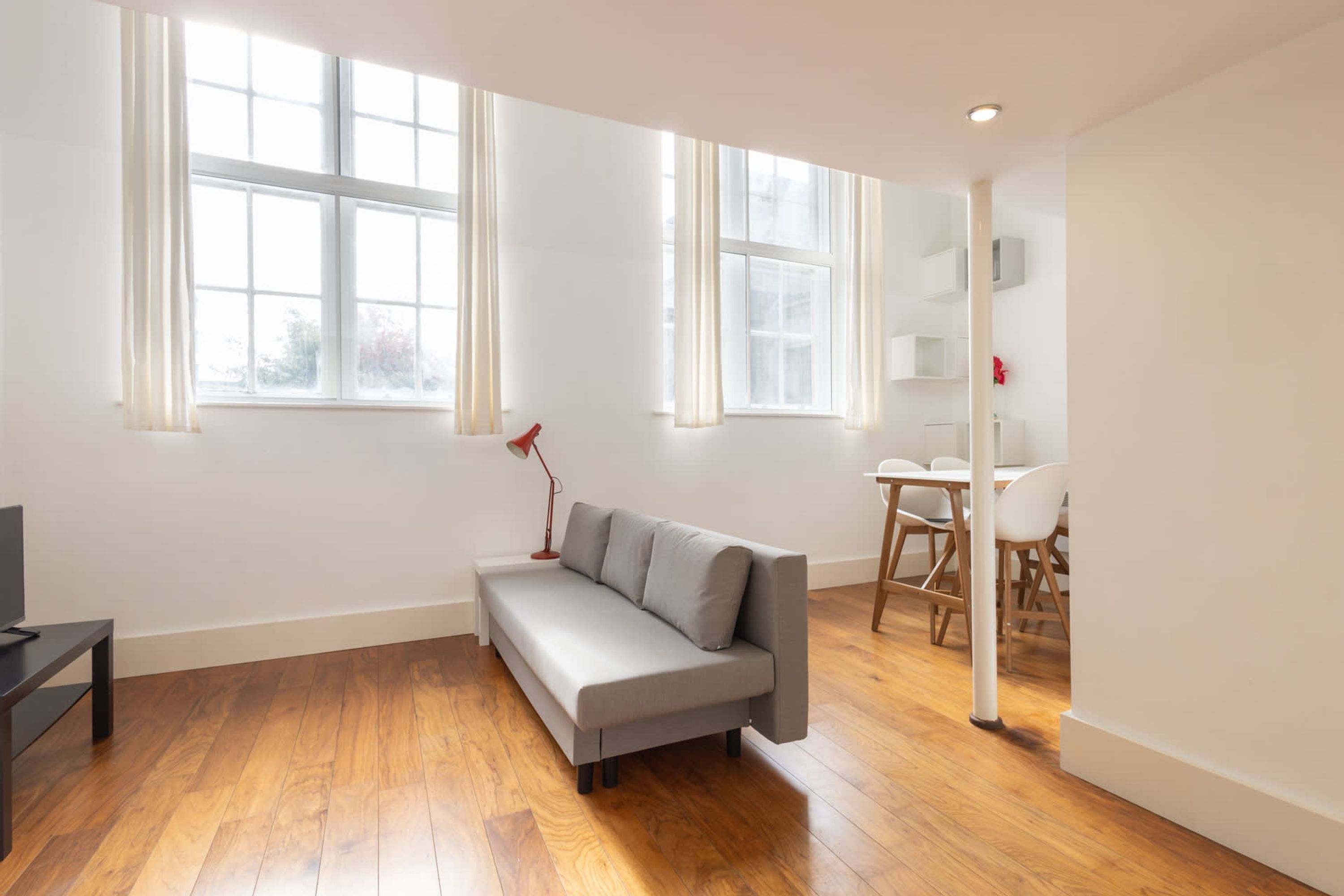 Un salon moderne avec un canapé gris, un plancher en bois et de grandes fenêtres.