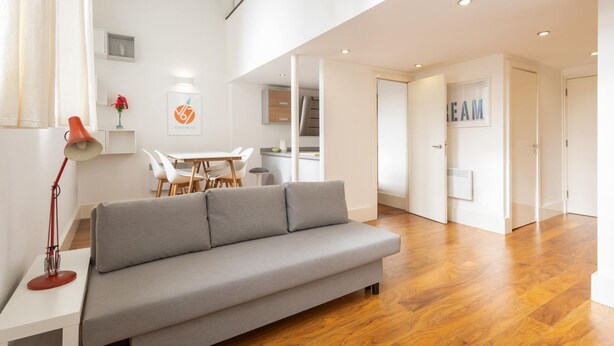 A modern living room with a grey sofa, wooden flooring, a dining area with a white table and chairs, and a staircase leading to an upper level. - Host Stay City Hall View (Sheffield)
