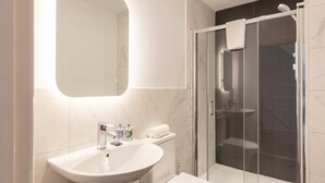 Une salle de bain moderne avec un lavabo blanc, des toilettes, une douche en verre et un grand miroir.