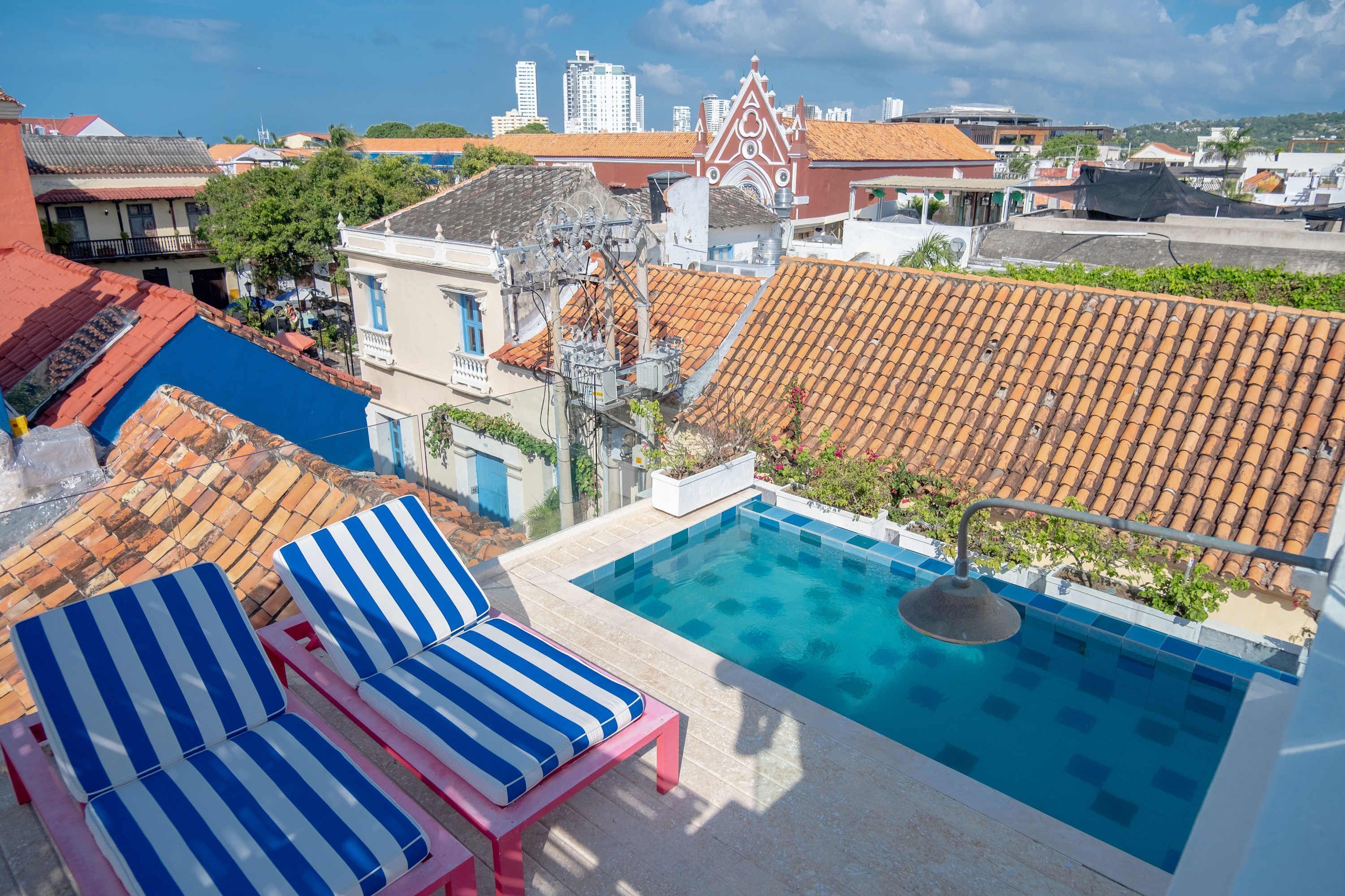 A rooftop pool with blue and white striped lounge chairs, a clear view of the cityscape, and a tiled roof.