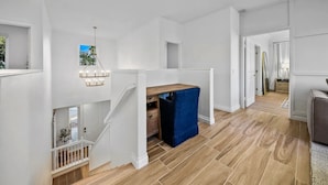 Un interior amplio con una escalera que lleva a una zona superior, un escritorio de madera y una silla azul.