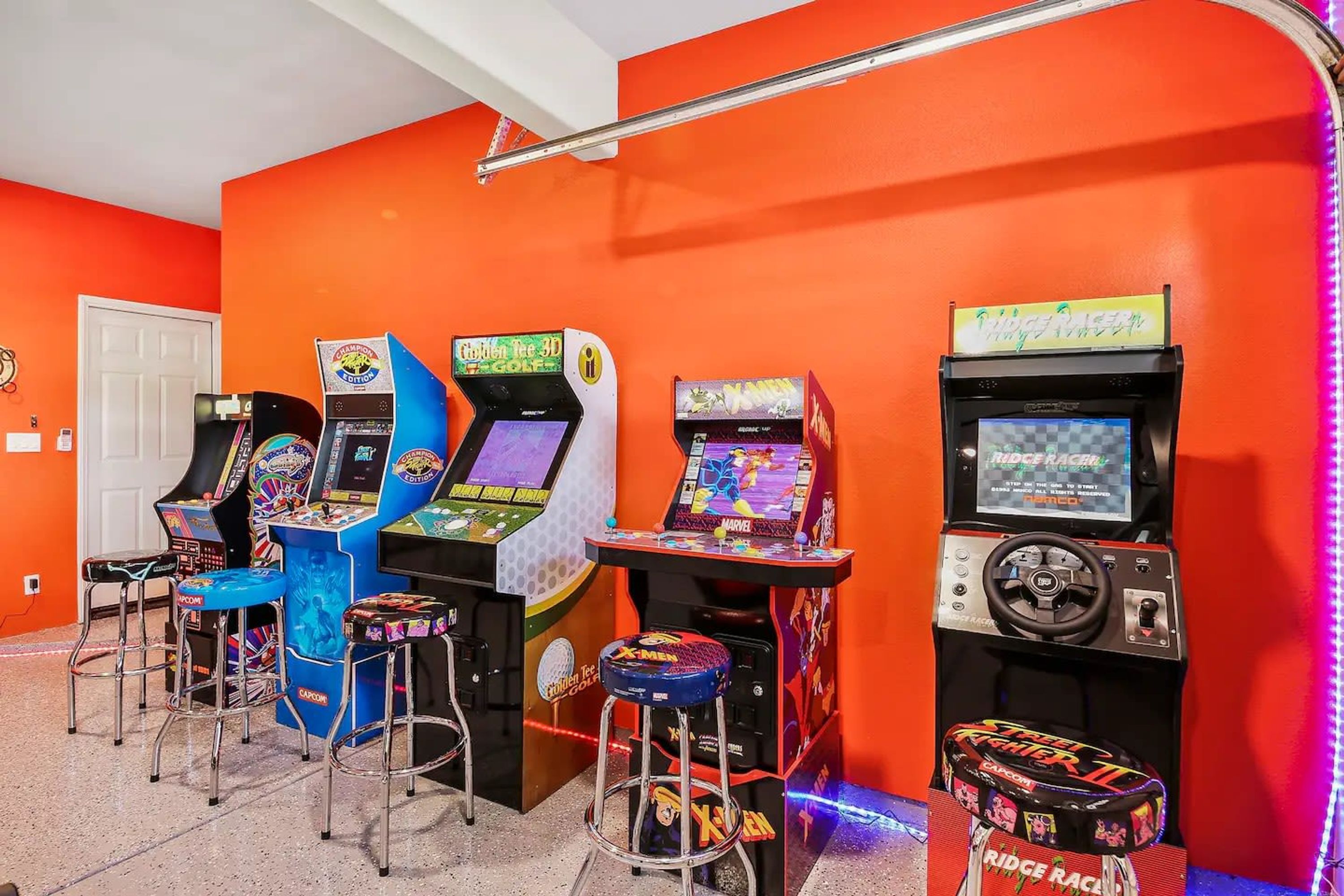 A room with four arcade machines, two bar stools, and a door.