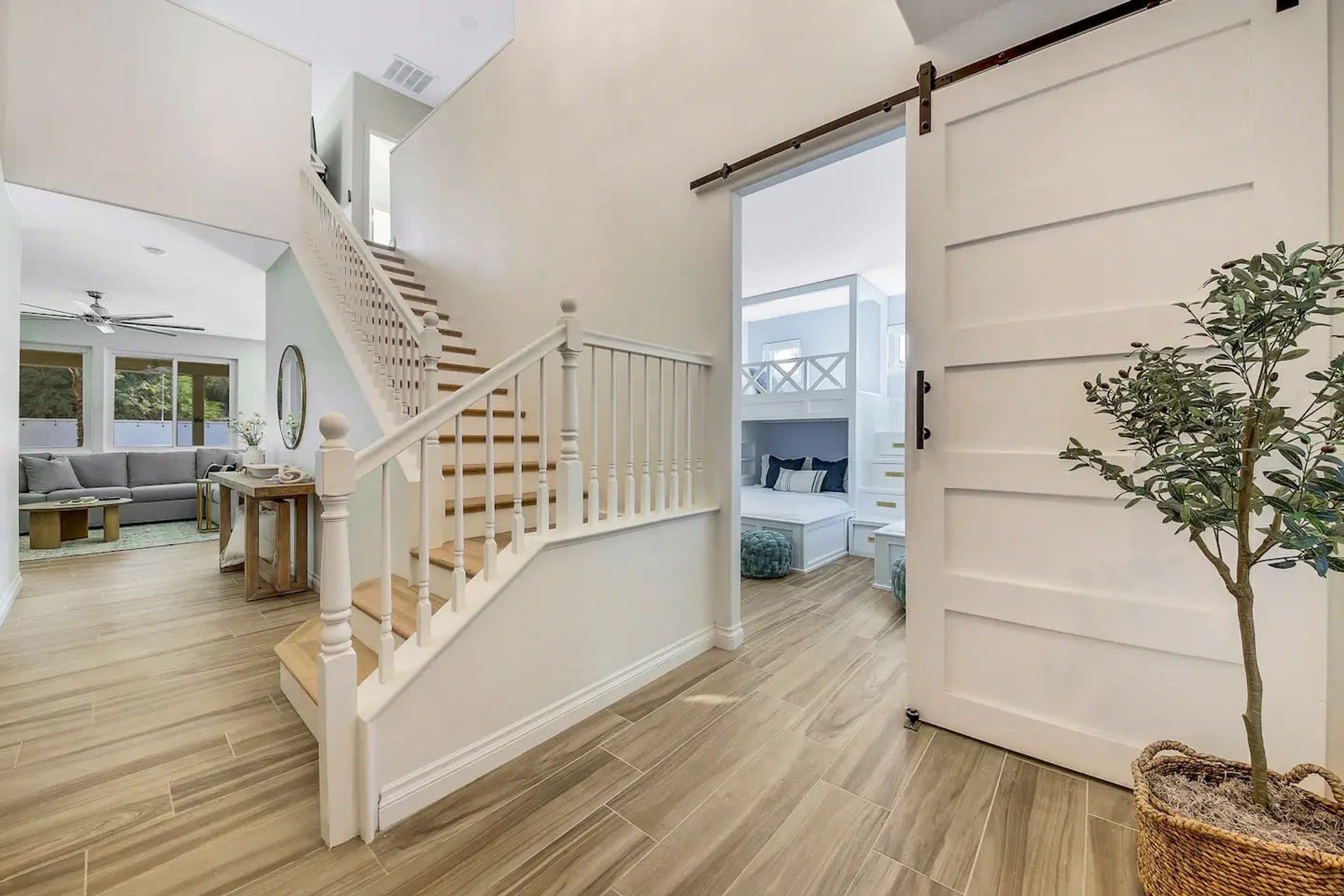A spacious living area with a wooden staircase, a large sliding door, and a potted plant.