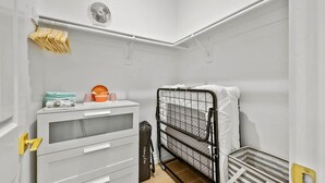 Una habitación pequeña y blanca con una cama litera, un aparador blanco con cajones, una mesita con artículos de aseo y un ventilador en el techo.