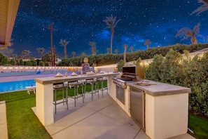 An outdoor patio with a pool, bar area, and grilling station. - WOW The Hamptons Pickleball Massive Pool Slide (Indio)