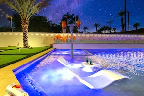 A nighttime pool area with a starry sky, a palm tree, and a sign that reads "Indio more Worry less." - WOW The Hamptons Pickleball Massive Pool Slide (Indio)