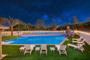 A swimming pool with a starry night sky, surrounded by greenery and white lounge chairs. - WOW The Hamptons Pickleball Massive Pool Slide (Indio)