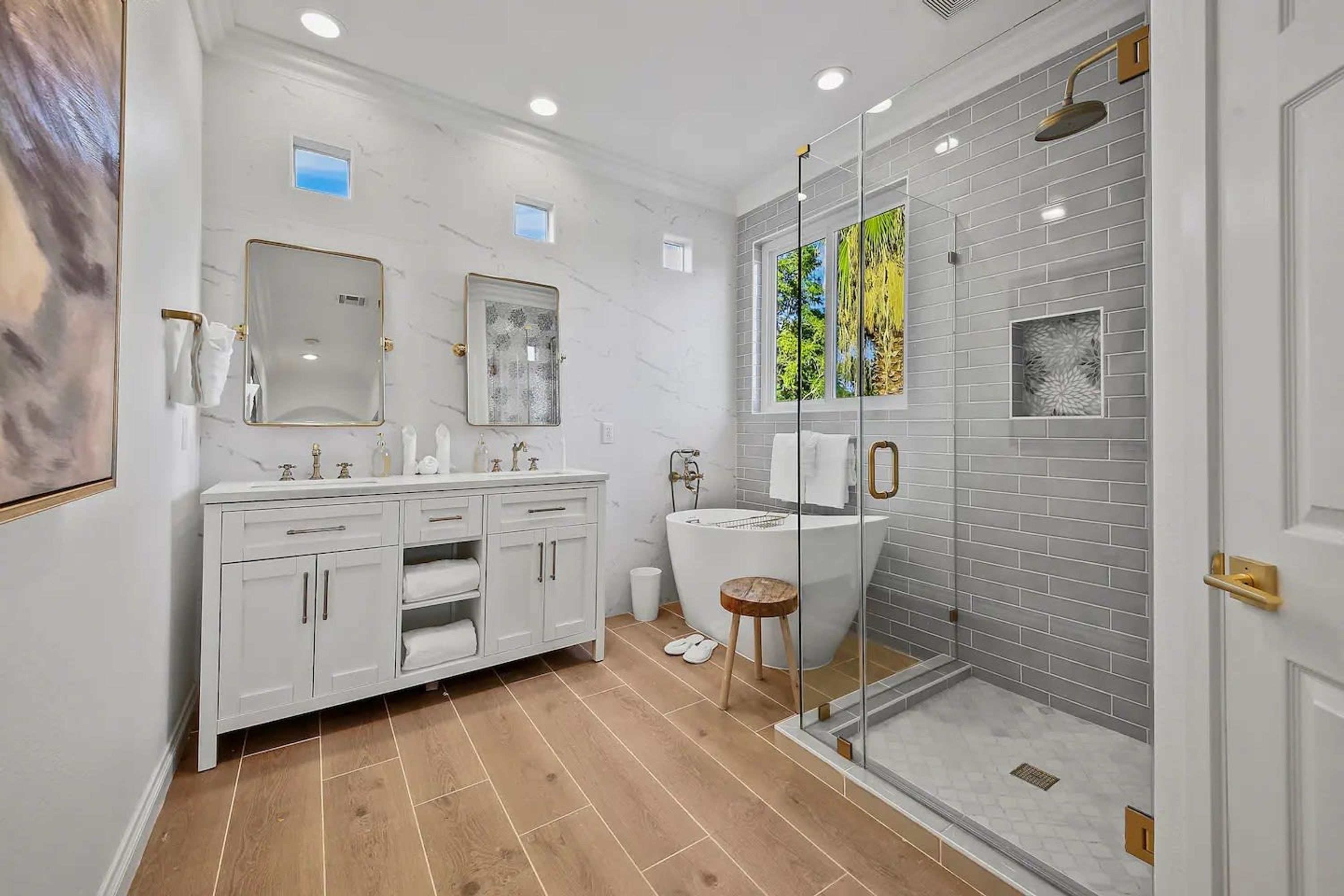 Une salle de bain moderne avec un meuble-lavabo blanc, une douche à parois de verre et une grande fenêtre.