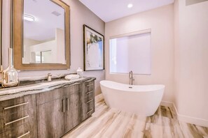 A modern bathroom with a freestanding bathtub, a large mirror, and a marble countertop.
